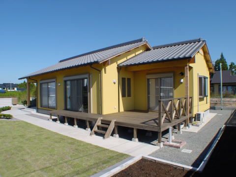 黄色い外壁と茶色のウッドデッキのある平屋住宅