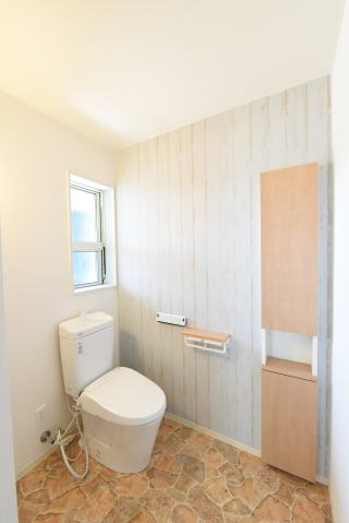 木目柄のアクセントクロスとサンドストーン調の床の壁埋め込み収納のあるトイレ