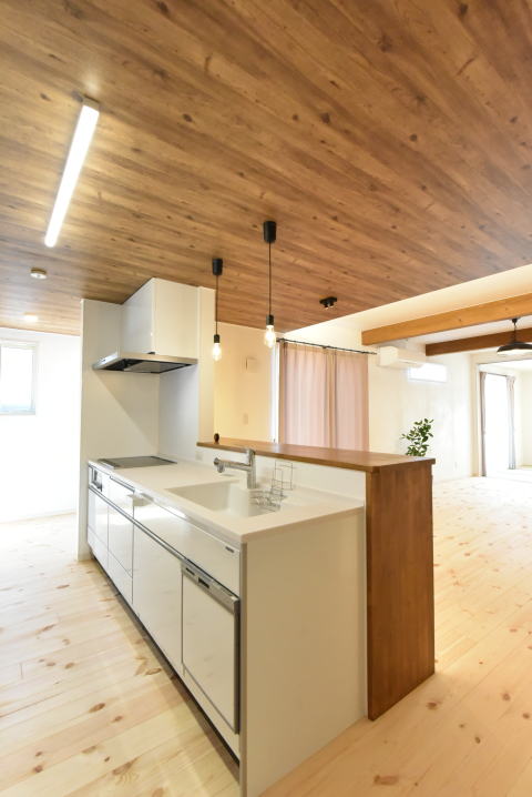 板張り調の天井クロスと白い対面キッチン