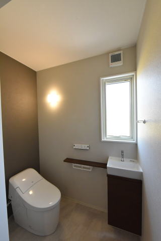 グレーのアクセントクロスと茶色の扉の手洗いカウンターのあるトイレ