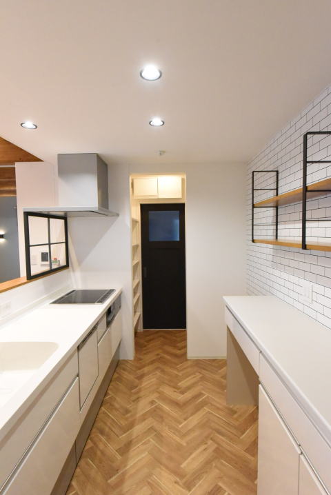 ヘリンボーン床とタイル調のアクセントクロスの白いキッチン