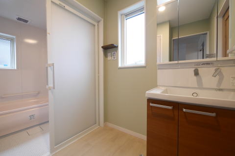 茶色い扉の洗面化粧台とグリーンのクロスの脱衣室