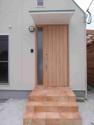 木目調の玄関ドアとテラコッタタイルの屋根付き玄関ポーチ