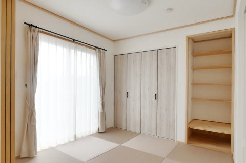 白い木目調の建具と棚がいっぱいの収納と薄いピンク色の畳の和室